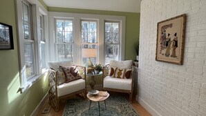 A cozy room with a white brick wall, a large window, a white sofa, a small round table, and a patterned rug.
