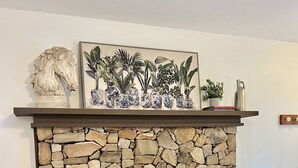 A stone fireplace with a black screen door, a shelf above holding a lion head sculpture, a framed plant art, and two decorative vases.