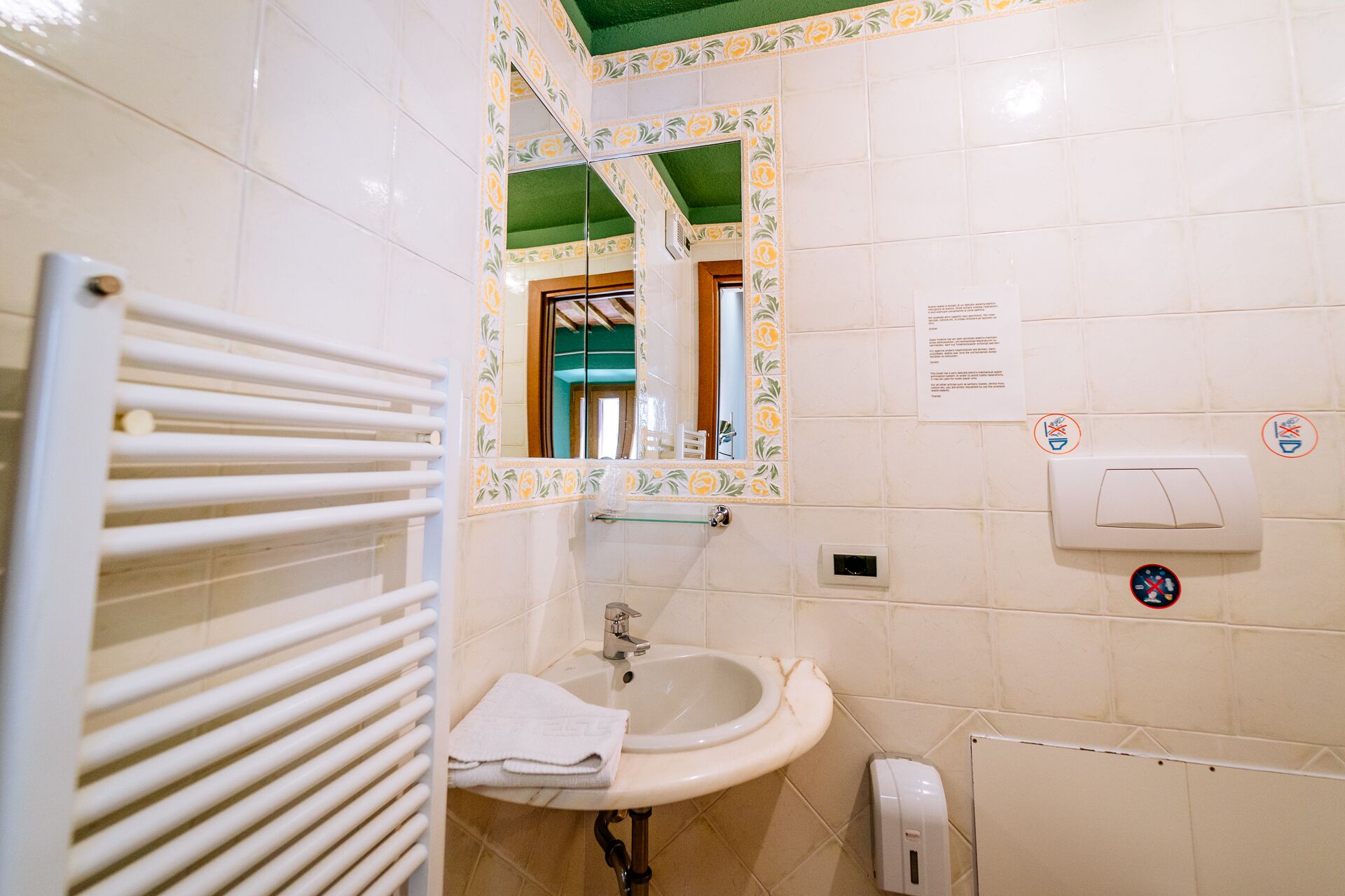 Un baño con lavamanos blanco, toallero, espejo y secador de manos.