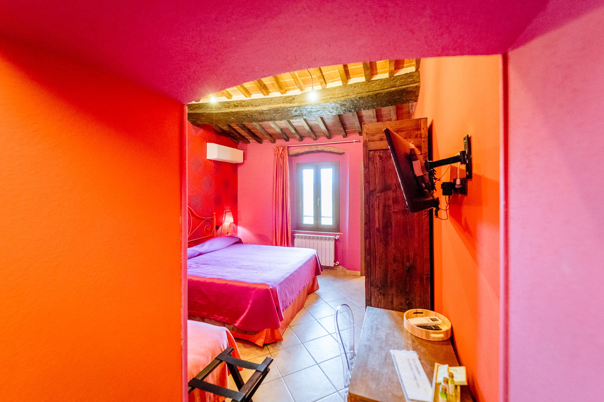 A bedroom with a bed, a window, a wooden ceiling, and a bathroom with a sink and mirror.