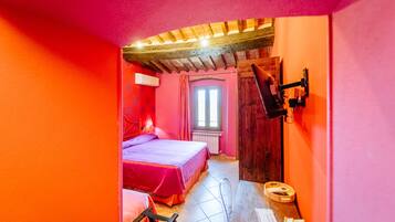 A bedroom with a bed, a window, a wooden ceiling, and a bathroom with a sink and mirror.