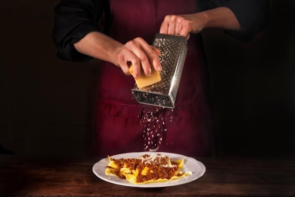 A person grating cheese over a dish.