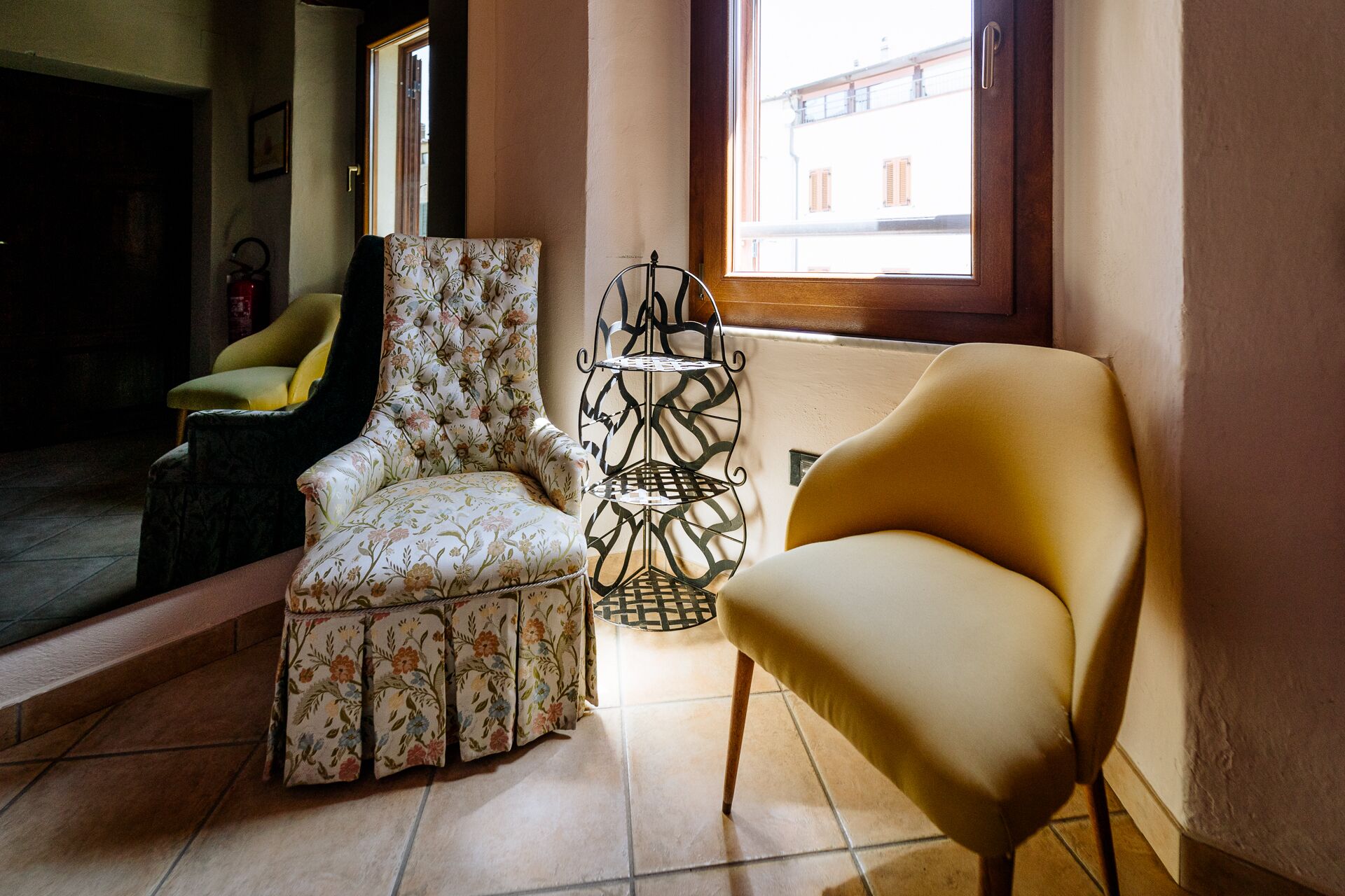 Una stanza con una poltrona floreale, una poltrona moderna e una mensola metallica decorativa.