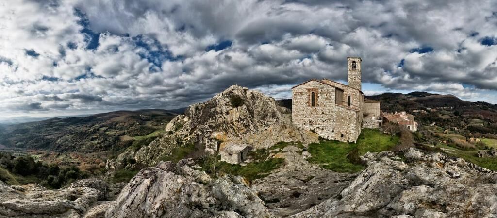 A stone building with a tower, surrounded by rocky terrain and hills.