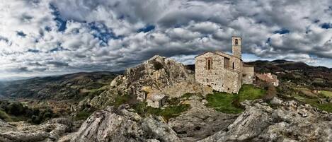 A stone building with a tower, surrounded by rocky terrain and hills.