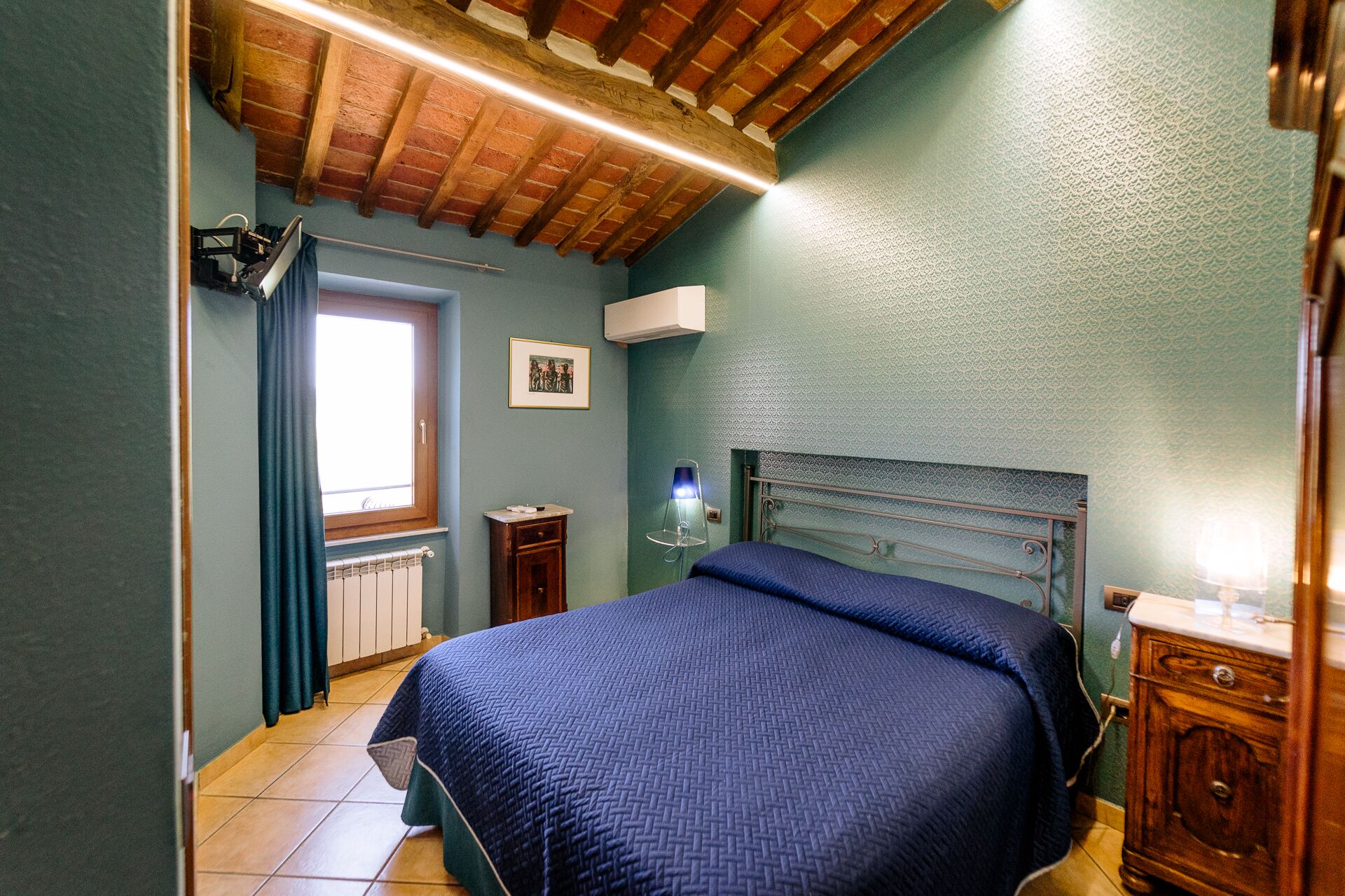 A bedroom with a bed, a radiator, a window, and a wooden ceiling.