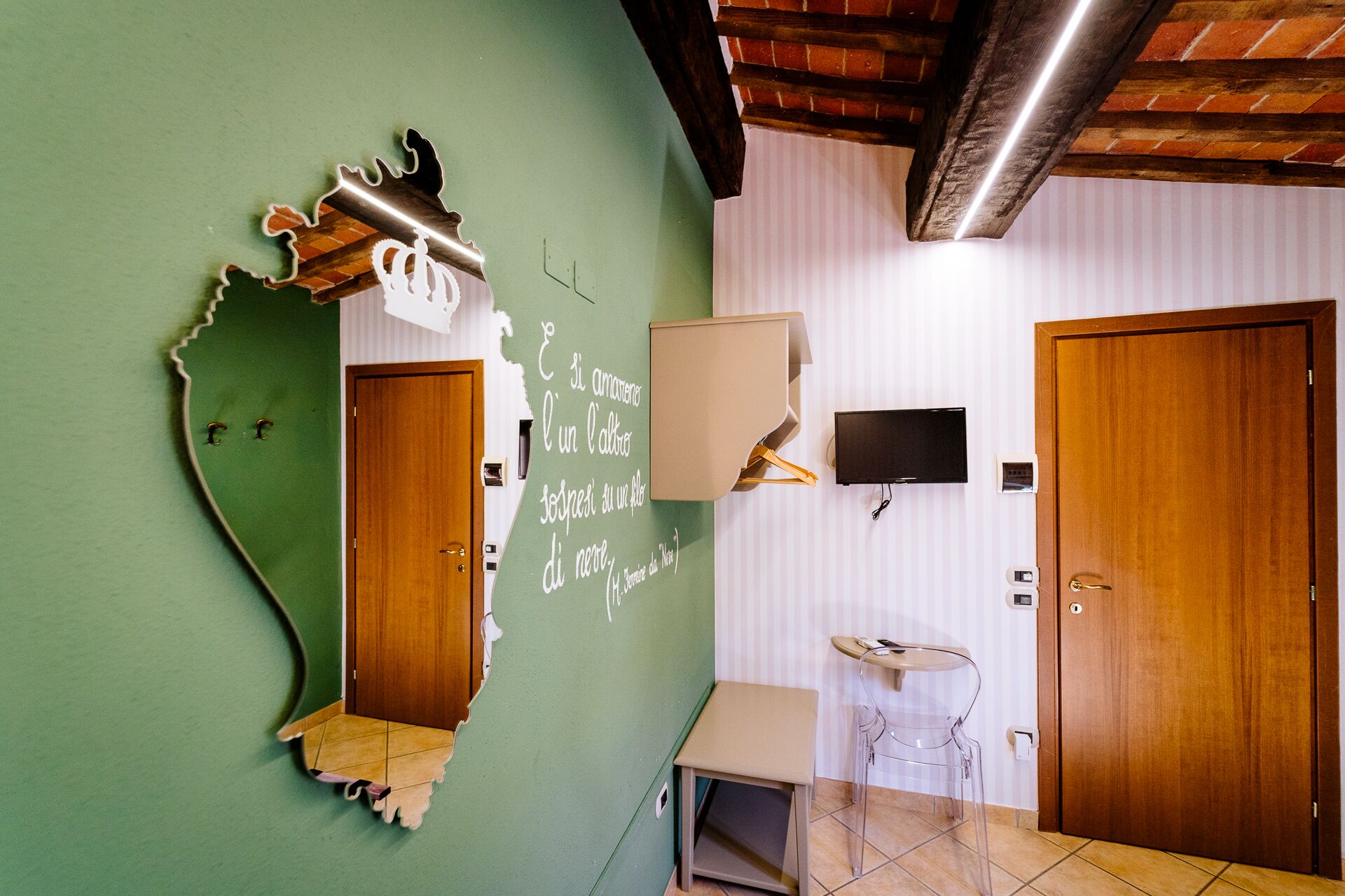 A room with a green wall, a wooden door, a small table, a chair, a mounted TV, and a ceiling light fixture.
