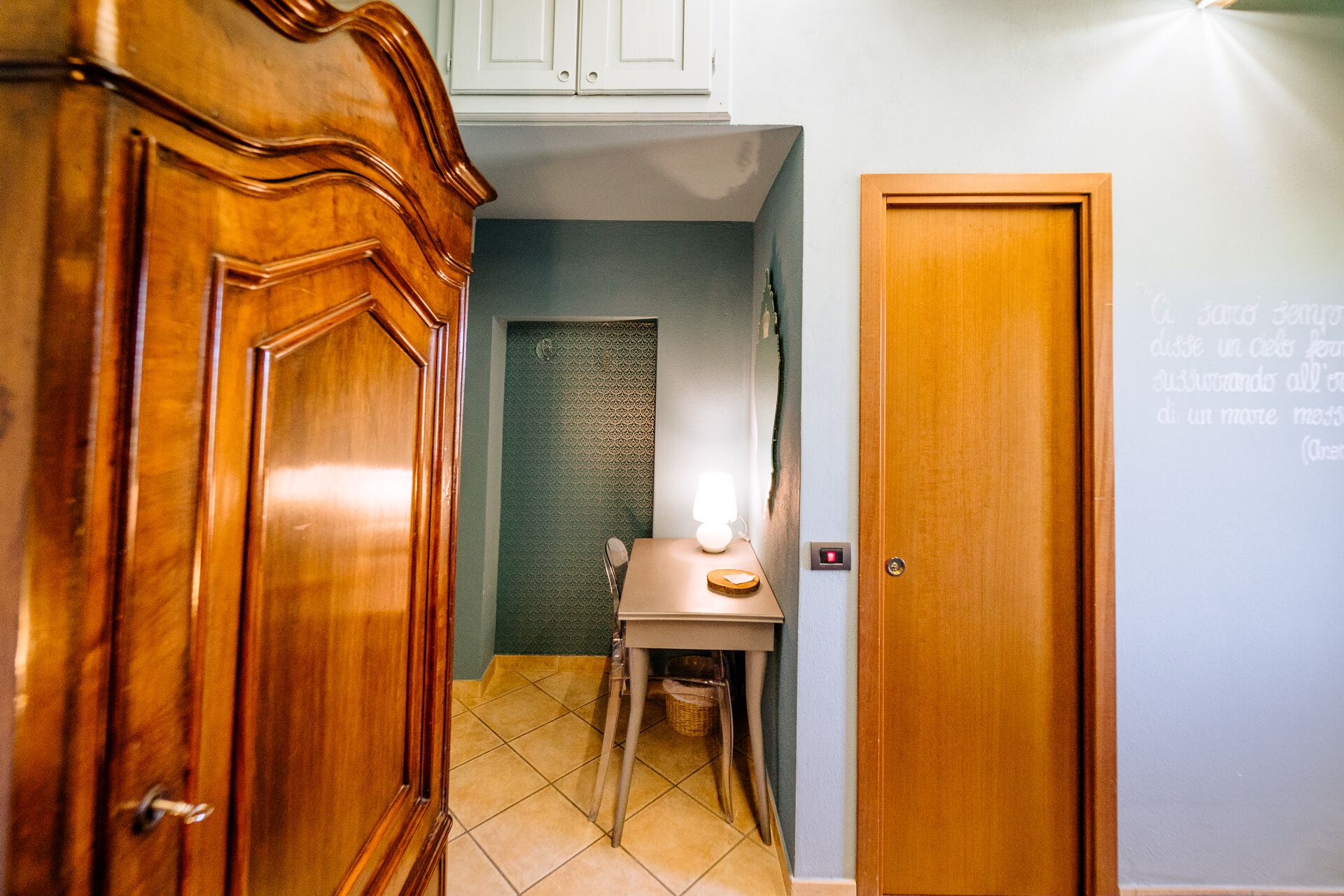 A hallway with a wooden door, a small table with a lamp, and a tiled floor.