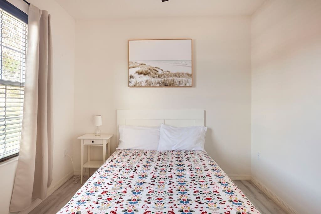 A bedroom with a bed, a nightstand, a lamp, and a window with curtains.