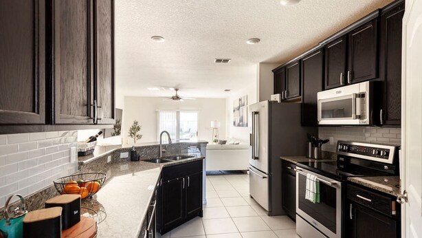 A modern kitchen with dark cabinetry, stainless steel appliances, and a granite countertop. - Modern 4 Bdr Home near Tradition Town Center (Port St. Lucie)