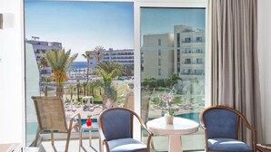 A balcony with two chairs, a small table, and a view of a pool and buildings. - Tsokkos Beach Hotel (Paralimni)