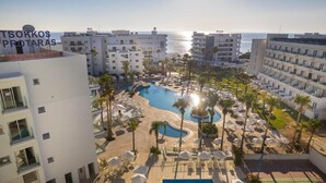 A resort with a swimming pool, palm trees, and a view of the sea. - Tsokkos Beach Hotel (Paralimni)
