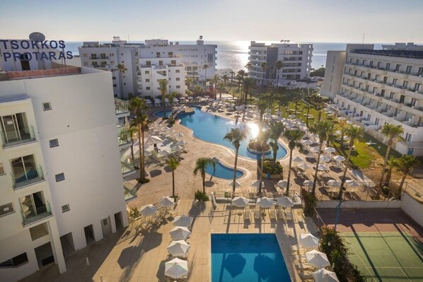 Un complexe hôtelier doté d’une piscine, de palmiers et offrant une vue sur la mer.