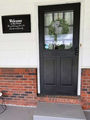 Puerta principal negra adornada con un adorno navideño y un cartel que dice 'Bienvenido a Nuestro Porche'.