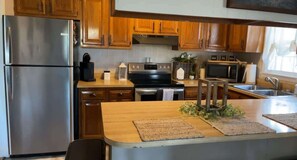 Cocina con armarios de madera, electrodomésticos de acero inoxidable, una isla de madera y un ventanal que proporciona luz natural.