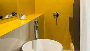 Un baño con una pared amarilla, un lavamanos blanco y una ducha.