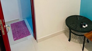 Una habitación con una puerta que da a un pasillo, una mesita con una silla y un equipo de aire acondicionado instalado en la pared.