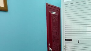 Una habitación con una puerta roja, una puerta blanca con un número y un ventanal pequeño sobre la puerta roja.