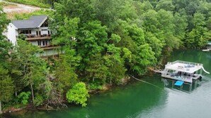 A house with a balcony overlooking a river, surrounded by dense forest. - 25% late summer discount! Lakefront | 2 slip covered dock | Hot tub | (Speedwell)