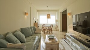 A living room with a sofa, dining table, chairs, a TV, and a lamp. - LucyZen! Stylish Apt, Athenian Riviera, near beach (Vouliagmeni)