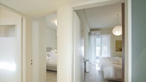 A hotel room with a bed, a bedside table, a lamp, and a window with curtains. - LucyZen! Stylish Apt, Athenian Riviera, near beach (Vouliagmeni)