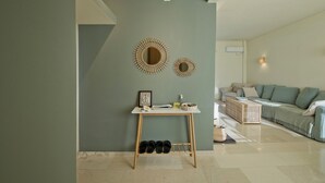 A living room with a green wall, a wooden table with shoes, a sofa, and two wall-mounted mirrors. - LucyZen! Stylish Apt, Athenian Riviera, near beach (Vouliagmeni)