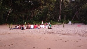A group of people sitting on the beach in a semi-circle, with trees and a few plastic chairs in the background. - The Water Melon House (Samaná)