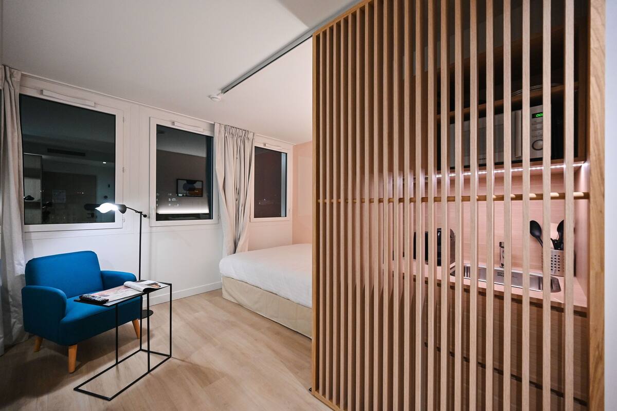 A modern room with a blue chair, a small table, a bed, and a wooden partition with shelves.