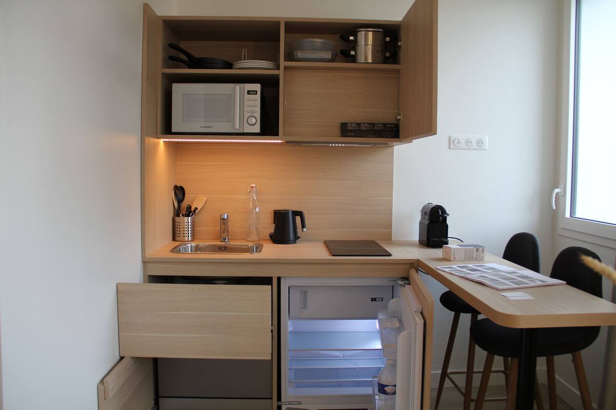 A compact kitchen with a microwave, kettle, and coffee maker, a small sink, and a dining area with chairs.