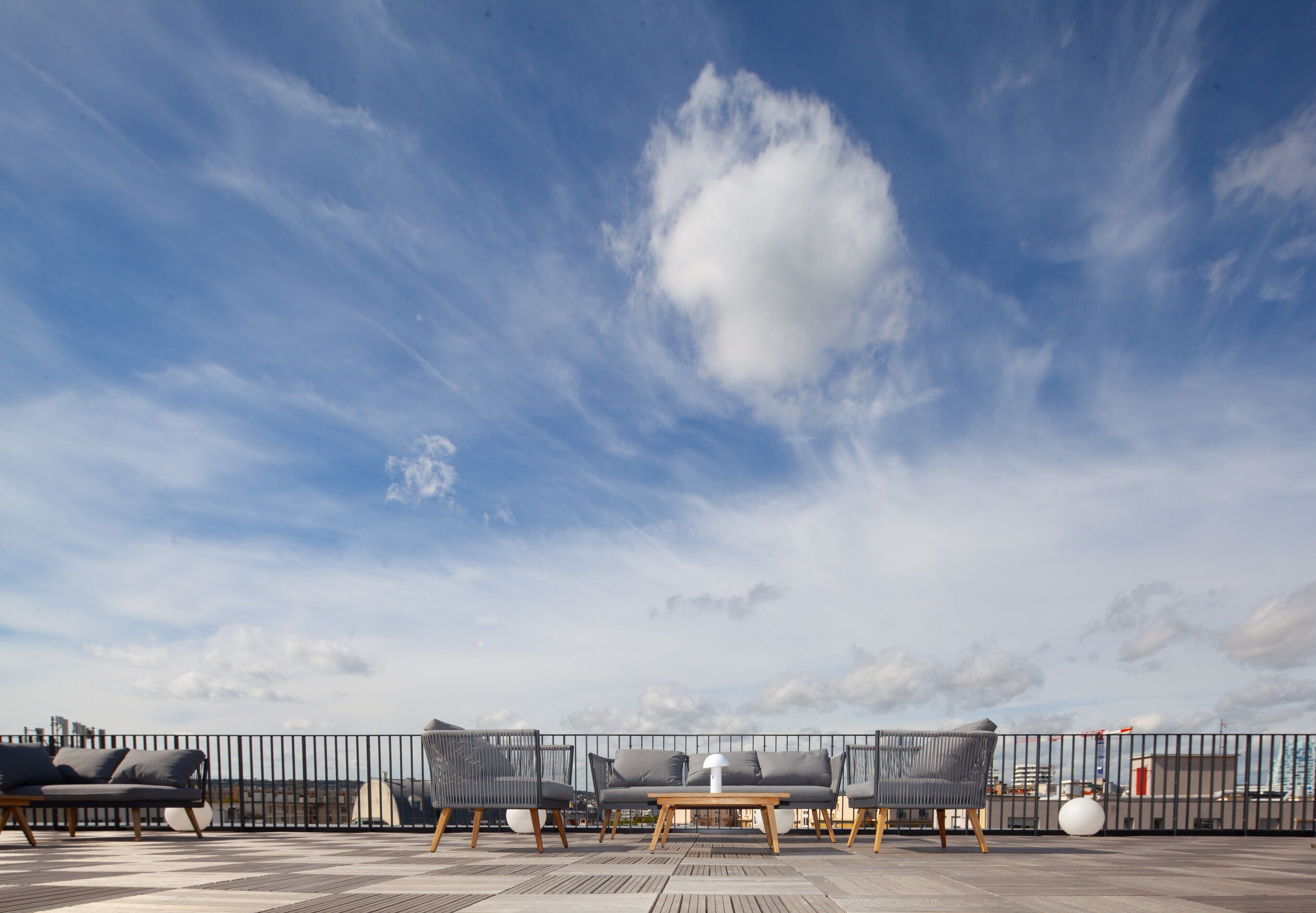 A rooftop terrace with a seating area featuring a table and chairs, a railing, and a view of the cityscape.