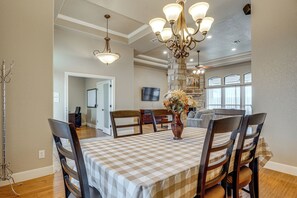 A dining area with a checkered tablecloth, wooden chairs, a vase with flowers, and a chandelier.