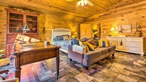A log cabin interior with a wooden ceiling, a bed with a headboard, a sofa, a desk, and a cabinet. - Pet-Friendly Cabot Cabin w/ Fenced Yard! (Cabot)