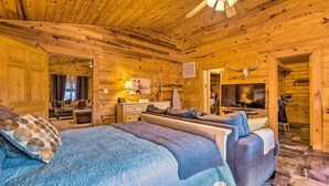 A log cabin-style bedroom with a large bed, a sofa, a TV, and a ceiling fan. - Pet-Friendly Cabot Cabin w/ Fenced Yard! (Cabot)