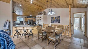Une cuisine moderne avec un plafond en bois, un coin repas avec une table et des chaises en bois, et un bar avec des tabourets.