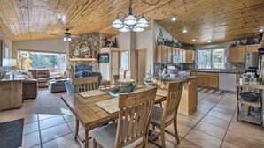 Un vaste espace de vie comprenant un coin repas avec une table et des chaises en bois, ainsi qu’une cuisine dotée de meubles en bois et d’un mur d’accent en pierre.