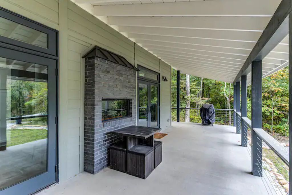 Un patio techado al aire libre con chimenea de piedra, ventanas amplias y piso de concreto.