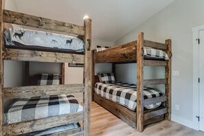 Quarto com beliches, design rústico em madeira, com duas camas e roupa de cama xadrez, além de um travesseiro com tema de veado.