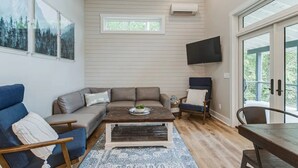 Ein gemütliches Wohnzimmer mit einer Couch, Sesseln, einem Couchtisch und einem an der Wand montierten Fernseher.