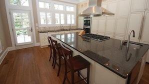 A kitchen with a large island, white cabinetry, and a stainless steel range hood. - Beach luxury at it's best!! (Rehoboth Beach)