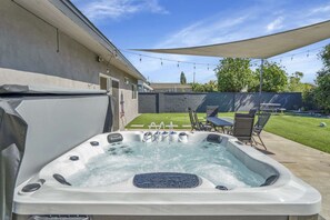 Un jacuzzi con múltiples chorros, rodeado por un patio con mobiliario exterior y una guirnalda de luces.
