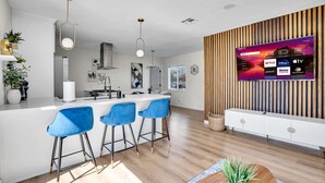 Une cuisine moderne dotée d’un coin bar, de lambris en bois et d’un grand téléviseur diffusant différents services de streaming.