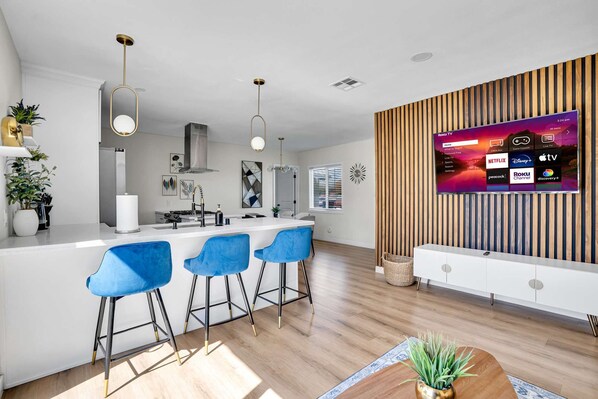 Cocina moderna con barra, paneles de madera y un televisor grande mostrando diferentes servicios de streaming.