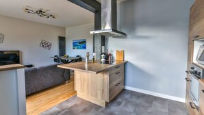 A modern kitchen with a central island, a built-in oven, and a stainless steel range hood. - Le Tropi'Cognac - Center - Terrace garden - 3 BR (Cognac)