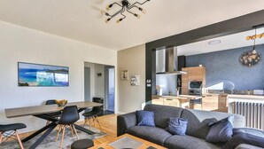 A modern living room with a grey sofa, wooden coffee table, and a dining area with a wooden table and chairs. - Le Tropi'Cognac - Center - Terrace garden - 3 BR (Cognac)