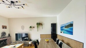 A modern living room with a wooden dining table, black chairs, a TV, and a fireplace. - Le Tropi'Cognac - Center - Terrace garden - 3 BR (Cognac)