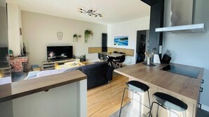 A modern kitchen with a central island, bar stools, and a dining area with a TV. - Le Tropi'Cognac - Center - Terrace garden - 3 BR (Cognac)
