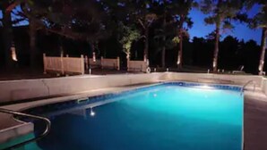 Una piscina con bordo curvo, circondata da una recinzione in legno e alberi.