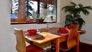 A dining area with a wooden table, red plates, and chairs. There is a window with a view of trees and a plant on the table. - 5 Star Upscale Unit Near Canyon Lodge (Mammoth Lakes)