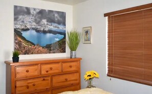 Enjoy a serene view of the surrounding landscape from the room's window, which looks out onto a beautiful mountainous lake. The room features a dresser and a potted plant, adding a touch of natural charm.