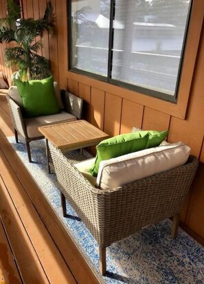 Relax in this inviting space with a wicker sofa, green and white pillows, and a small table.